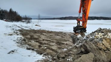 Meijerinrannan pilaantuneen maan puhdistus, kaivinkone ja Kiteenjärven rantaa näkyvissä talvisessa asussa