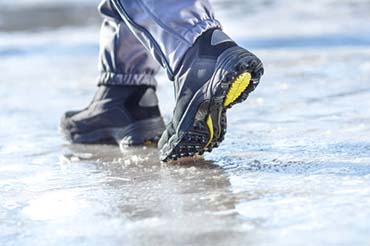 Kuvassa henkilö kulkee jäisellä järvenpinnalla. Kuva on otettu päivällä, aurinkoisella säällä. Kuvassa näkyy jäätä ja kengät.