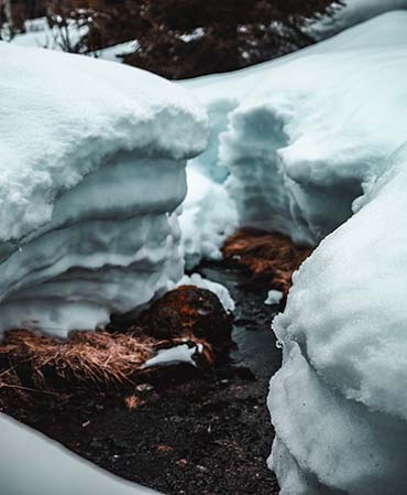 Kuvassa talvinen puro, jossa virtaa sulamisvettä ja kuvassa näkyy myös jonkin verran lunta. Kuva on otettu keväällä luonnossa. 