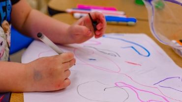 Lapsen kädet piirtämässä värikästä kuvaa.